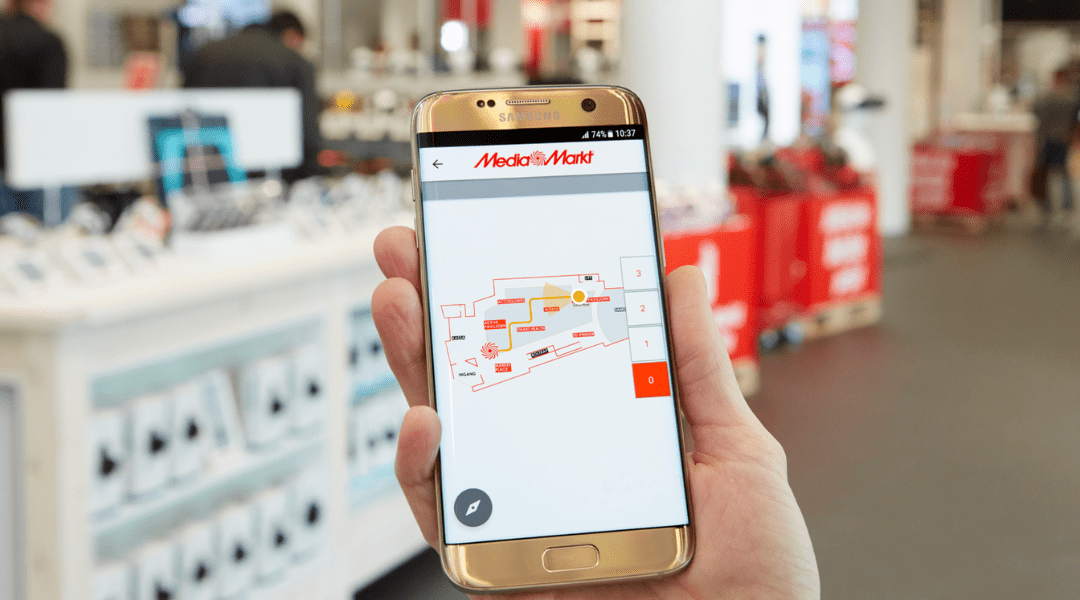 Una mano sostiene un teléfono móvil con el mapa de una tienda MediaMarkt.