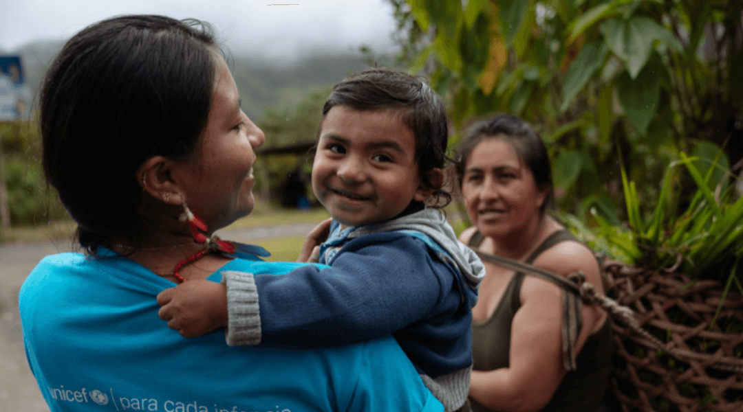 A woman in an UNICEF t-shirt holding a smiling child with another woman